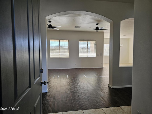 unfurnished room featuring visible vents, baseboards, ceiling fan, wood finished floors, and arched walkways