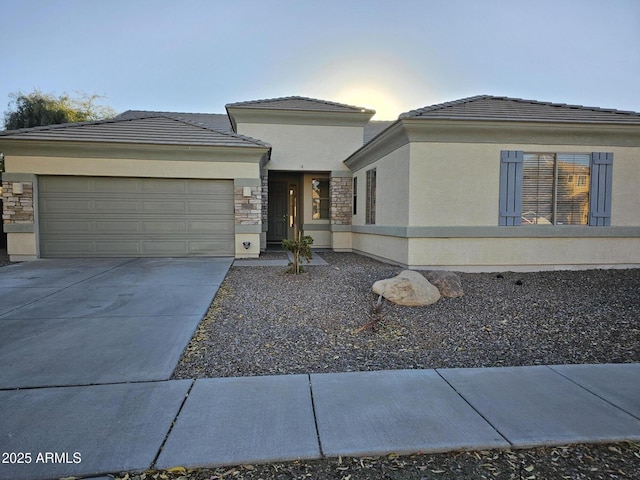 prairie-style home with stucco siding, stone siding, concrete driveway, an attached garage, and a tiled roof