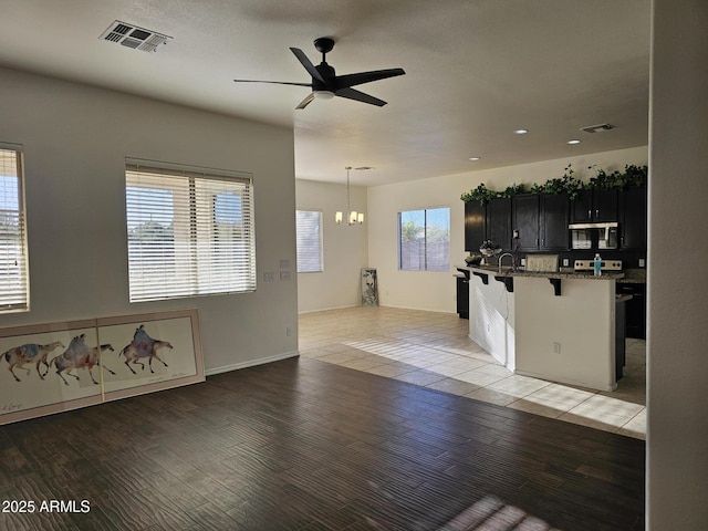 unfurnished living room featuring a sink, visible vents, light wood-style floors, and ceiling fan with notable chandelier