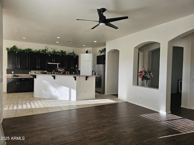 kitchen with stainless steel fridge, light wood-style floors, a breakfast bar, and dark cabinetry