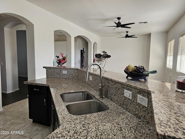 kitchen with visible vents, a sink, light stone counters, light tile patterned flooring, and dark cabinets