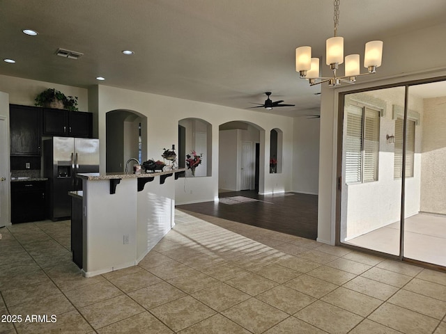 kitchen featuring light tile patterned floors, light stone counters, dark cabinetry, and stainless steel refrigerator with ice dispenser