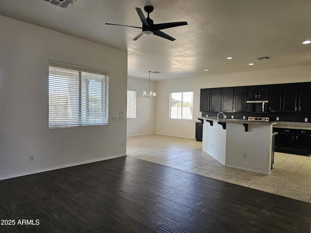 kitchen with a kitchen breakfast bar, light hardwood / wood-style flooring, ceiling fan with notable chandelier, hanging light fixtures, and a kitchen island with sink