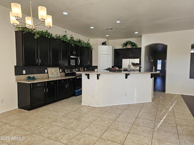 kitchen featuring a breakfast bar, visible vents, dark cabinets, and appliances with stainless steel finishes