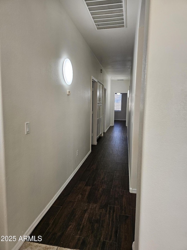 hall with visible vents, baseboards, and dark wood-style flooring