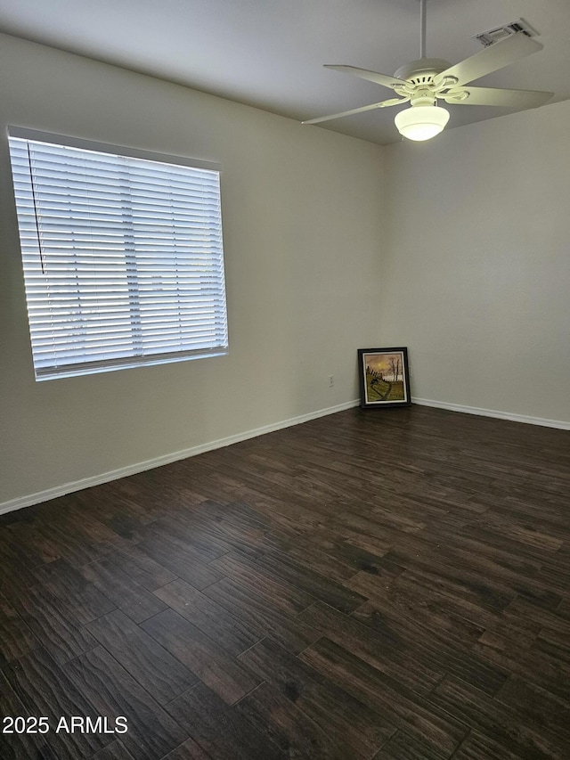 empty room with dark wood-type flooring, a ceiling fan, visible vents, and baseboards