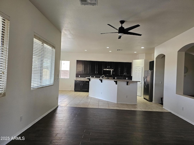 kitchen with an island with sink, a ceiling fan, stainless steel appliances, light wood-style floors, and a breakfast bar area