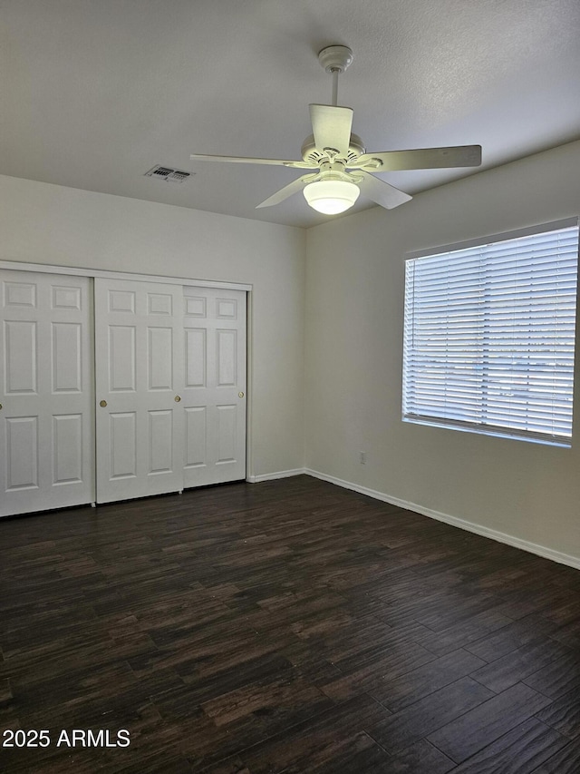 unfurnished bedroom featuring a closet, baseboards, visible vents, and dark wood-style floors