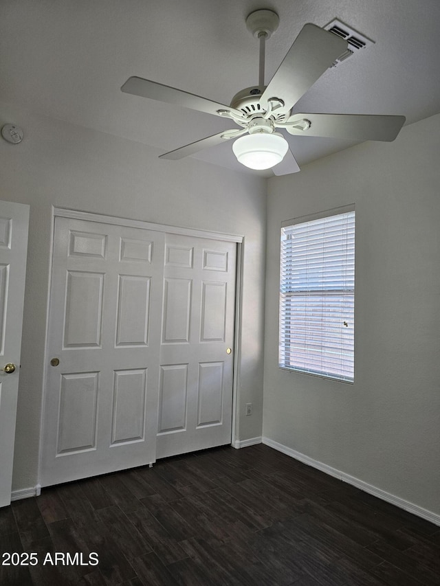 unfurnished bedroom with dark wood-style floors, visible vents, baseboards, ceiling fan, and a closet