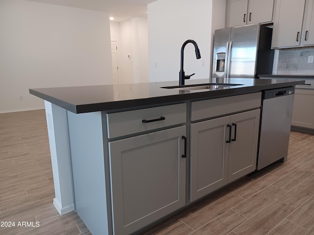 kitchen with stainless steel appliances, gray cabinets, and an island with sink