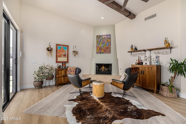 sitting room featuring a lit fireplace, beam ceiling, light wood-type flooring, and visible vents