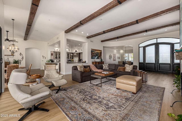 living room with arched walkways, french doors, beam ceiling, a notable chandelier, and light wood-type flooring