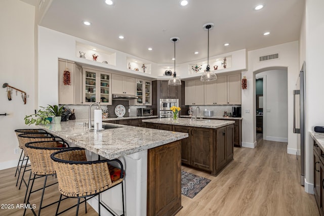 kitchen featuring arched walkways, a kitchen island with sink, a sink, a peninsula, and a kitchen breakfast bar