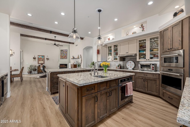 kitchen featuring arched walkways, decorative backsplash, an island with sink, light wood-type flooring, and a sink