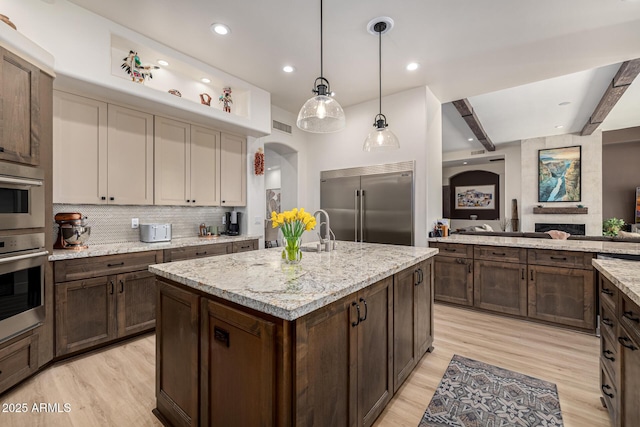 kitchen with light wood finished floors, dark brown cabinets, stainless steel built in refrigerator, and backsplash