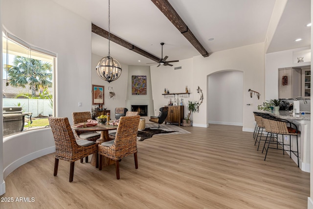 dining space featuring light wood finished floors, a fireplace, arched walkways, and beam ceiling