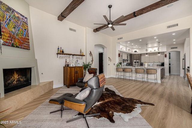 living room with a warm lit fireplace, visible vents, arched walkways, and beamed ceiling