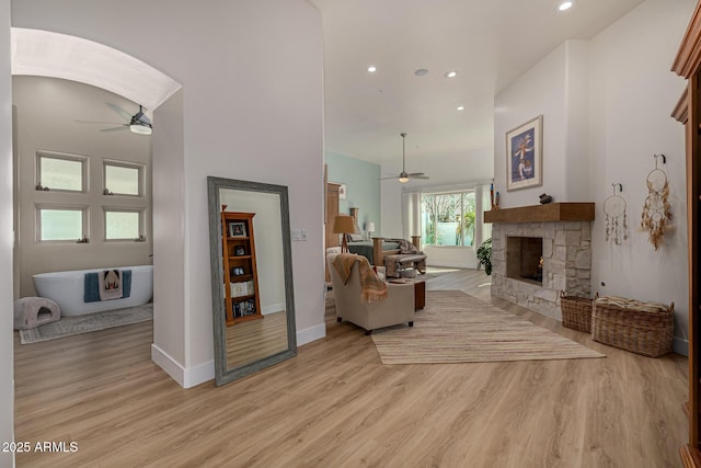 living area featuring a ceiling fan, light wood-type flooring, and a stone fireplace