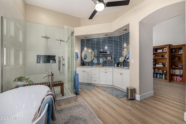 full bath with tile walls, double vanity, a soaking tub, a shower stall, and wood finished floors