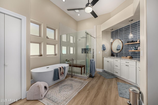 bathroom with wood finished floors, a ceiling fan, vanity, a freestanding bath, and a shower stall