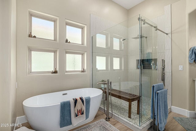 full bath featuring a wealth of natural light, a freestanding bath, a shower stall, and wood finished floors