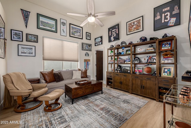 living area with ceiling fan, a high ceiling, and wood finished floors