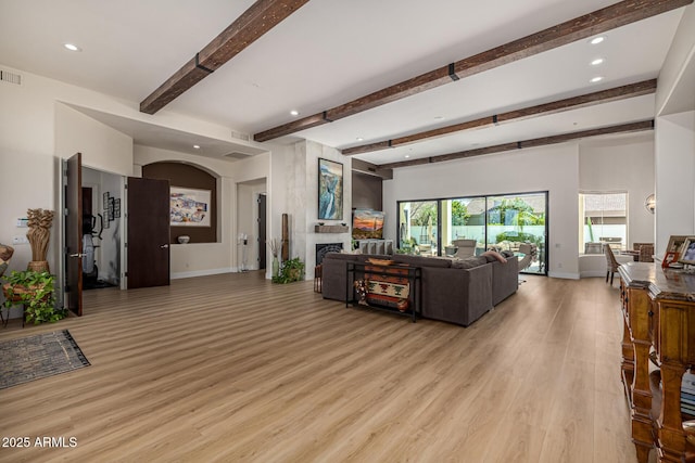 living area featuring light wood-type flooring, a large fireplace, baseboards, and beam ceiling