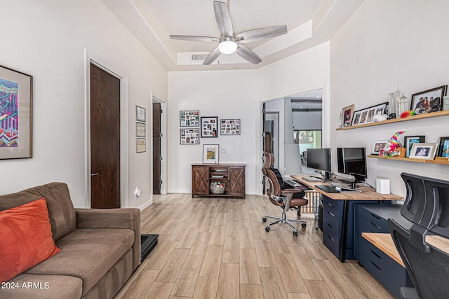 office with light wood-style flooring, visible vents, baseboards, a ceiling fan, and a raised ceiling