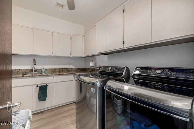 clothes washing area with washing machine and clothes dryer, cabinet space, visible vents, light wood-style flooring, and a sink