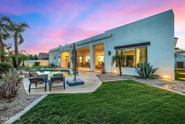 back of house at dusk featuring a fenced in pool, a yard, stucco siding, a patio area, and fence