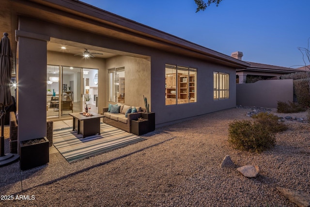 back house at dusk featuring ceiling fan, a patio, and an outdoor living space with a fire pit