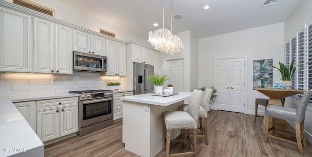 kitchen with light hardwood / wood-style floors, appliances with stainless steel finishes, tasteful backsplash, decorative light fixtures, and a kitchen island