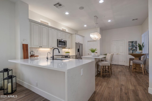 kitchen with kitchen peninsula, hanging light fixtures, sink, a breakfast bar area, and stainless steel appliances