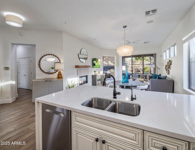 kitchen with light stone countertops, dishwasher, sink, decorative light fixtures, and light hardwood / wood-style flooring