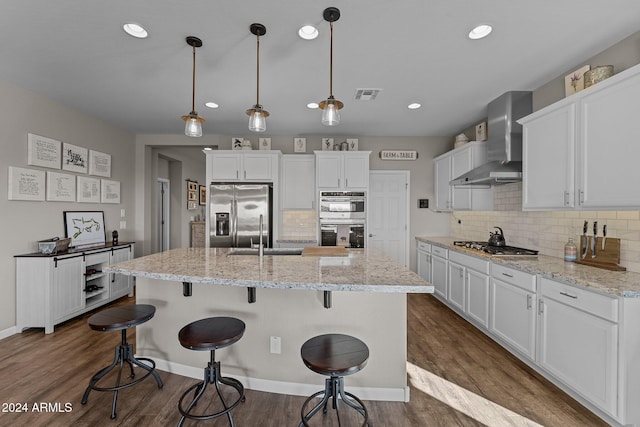 kitchen featuring stainless steel appliances, white cabinetry, wall chimney range hood, dark hardwood / wood-style floors, and an island with sink