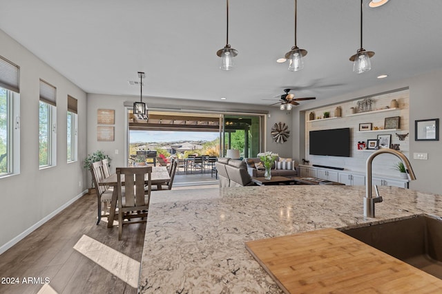 kitchen with dark wood-type flooring, hanging light fixtures, sink, ceiling fan, and light stone countertops