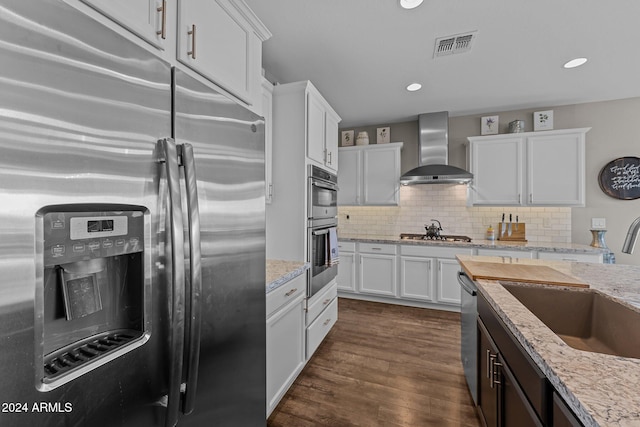 kitchen featuring stainless steel appliances, dark hardwood / wood-style flooring, white cabinets, wall chimney exhaust hood, and light stone countertops