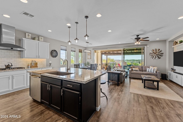 kitchen featuring hardwood / wood-style flooring, a center island with sink, sink, white cabinets, and wall chimney range hood