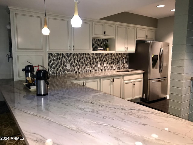 kitchen with decorative light fixtures, tasteful backsplash, sink, light stone counters, and stainless steel refrigerator with ice dispenser