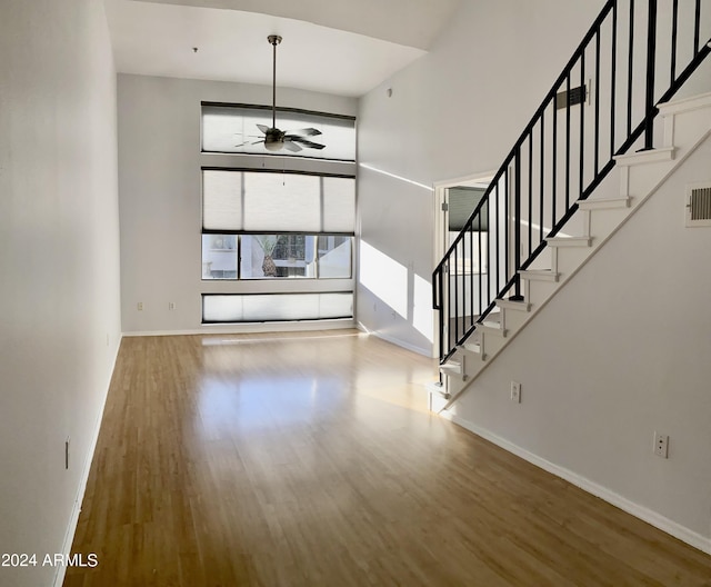 unfurnished living room with hardwood / wood-style flooring, ceiling fan, and a towering ceiling