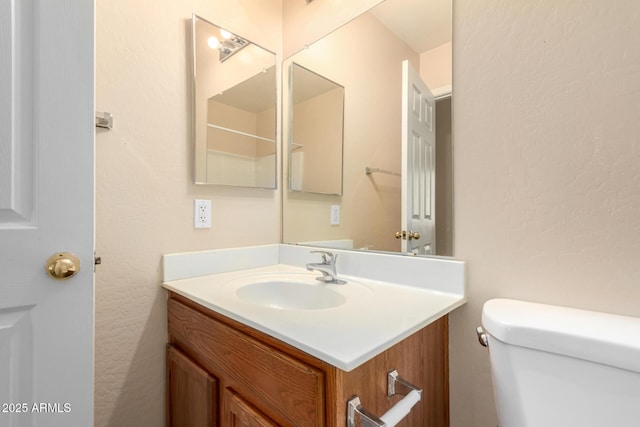 half bath featuring vanity, toilet, and a textured wall