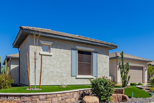 view of side of property with stucco siding, a lawn, and a garage