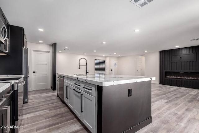 3008 W Michigan Ave, Phoenix, AZ 85053 - kitchen featuring a sink, electric range oven, an island with sink, light wood-type flooring, and visible vents