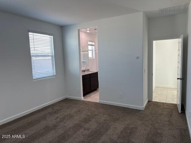 38055 W Excussare Way, Maricopa, AZ 85138 - unfurnished bedroom with light colored carpet, baseboards, a sink, and ensuite bathroom