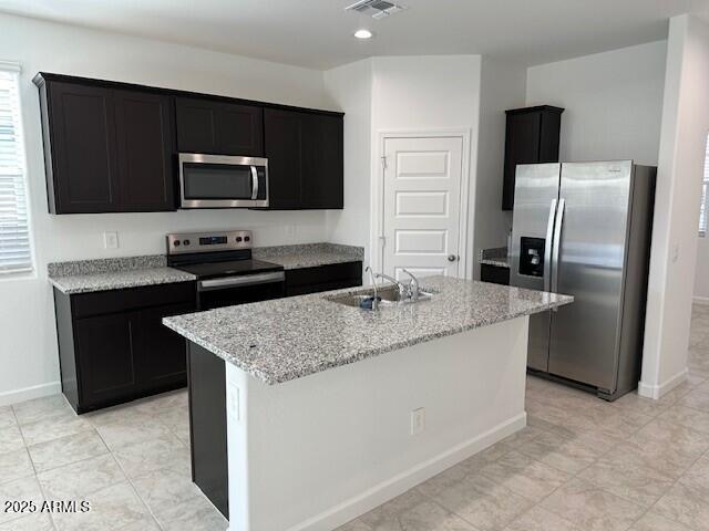 38055 W Excussare Way, Maricopa, AZ 85138 - kitchen featuring stainless steel appliances, a sink, dark cabinetry, baseboards, and light stone countertops
