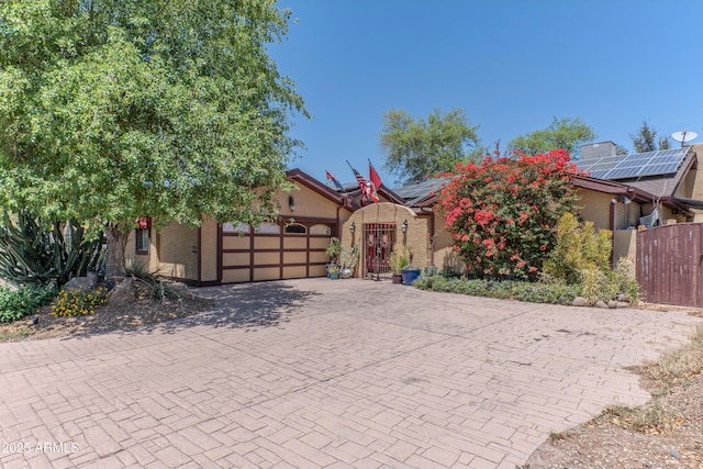1702 W Monterosa St W, Phoenix, AZ 85015 - view of property hidden behind natural elements featuring an attached garage, roof mounted solar panels, decorative driveway, stucco siding, and a gate