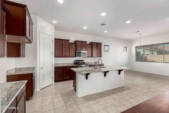 kitchen with sink, stainless steel appliances, light stone counters, a kitchen island with sink, and a breakfast bar