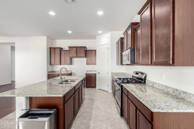 kitchen with light stone counters, stainless steel appliances, a kitchen island with sink, sink, and light tile patterned flooring