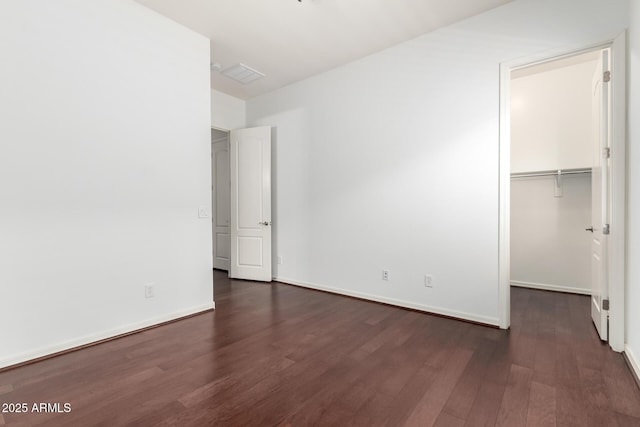 unfurnished bedroom with a spacious closet, a closet, and dark wood-type flooring