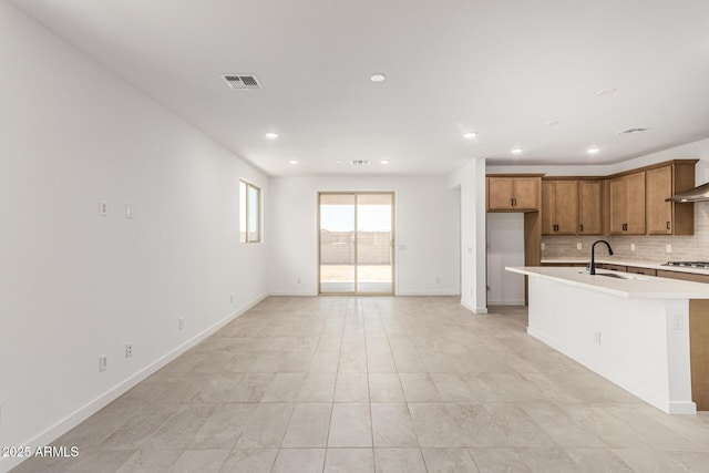 kitchen with a sink, backsplash, brown cabinetry, light countertops, and stainless steel gas cooktop